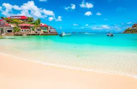 St Martin base showing azure blue waters on a beach with a bright blue sky with a couple boats on the water